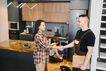 Happy young woman shaking hand of plumber after repairing workの写真素材