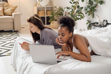 Young females using laptop and smartphone in bedの写真素材
