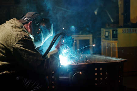 Worker in protective mask using angle grinder in workshopの写真素材