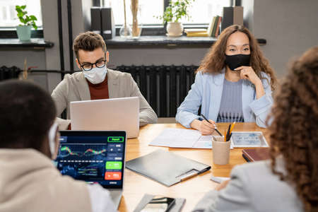 Group of young intercultural managers in protective masks working in office