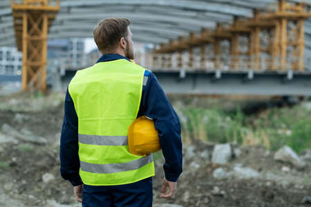 Rear view of builder in reflective clothing standing on construction site and working