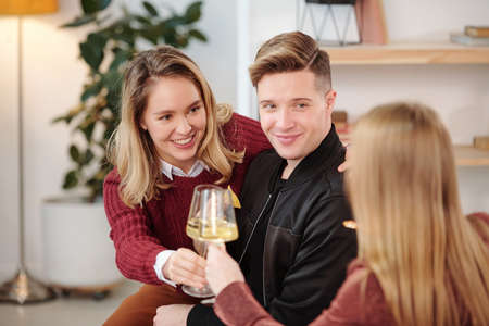 Group of young cheerful intercultural friends in smart casualwear gathered around small white round...