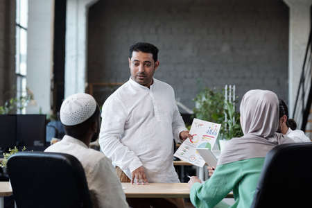 Confident businessman with financial paper looking at one of colleagues during discussion of dataの写真素材