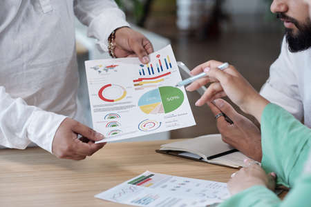 Hands of economists discussing financial document by workplace at meeting