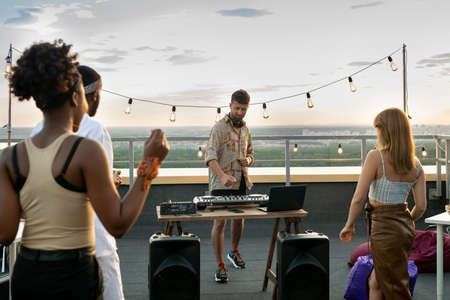 Intercultural friends dancing in front of deejay at rooftop partyの写真素材
