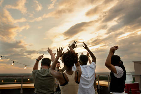 Rear view of young intercultural friends enjoying outdoor party on top of roofの写真素材