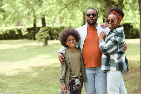 Affectionate African family of three standing in park against green lawnの写真素材