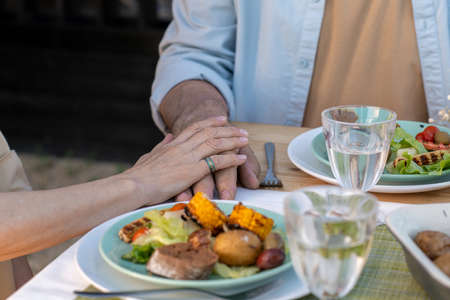 Hands of mature affectionate couple sitting by served table and having dinnerの写真素材