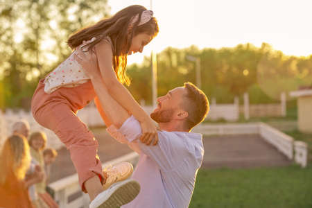 Happy young man holding cute little daughter during play in the countryside