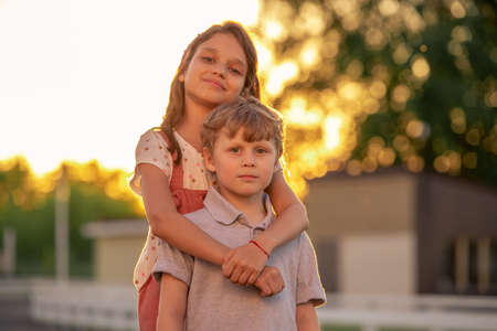 Cute little girl embracing her brother in front of camera outdoors