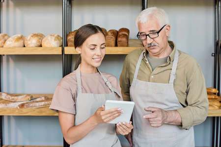 Two contemporary bakers consulting about prices of their products by workplaceの写真素材