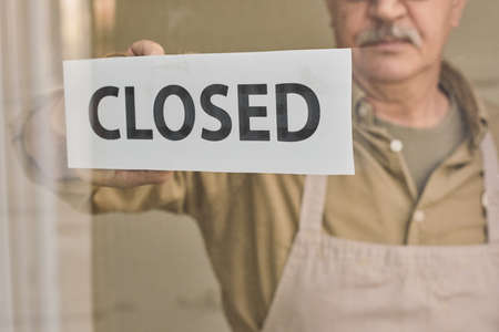 Signboard closed being hung by aged owner of cafe, store or bakeryの写真素材