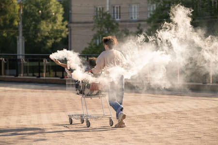 Ecstatic teenage dates having fun with firecrackers while guy pushing shopping cart with his...