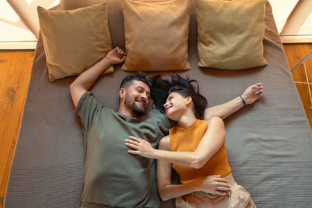 Young restful couple lying on bed with three cushions during summer vacationの写真素材