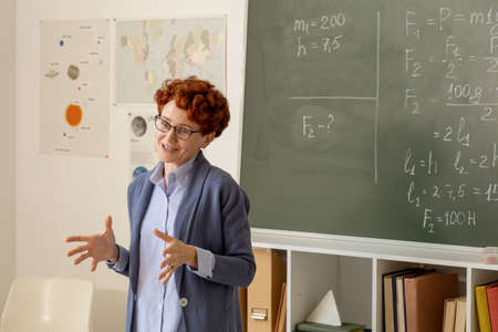 Young successful teacher explaining main points of subject by blackboard with physical formulasの写真素材