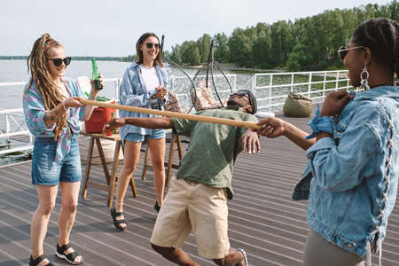 Young man bending backwards to walk under vertical bar in hands of his friend to win limbo game