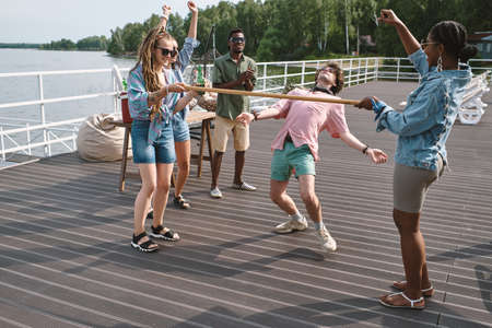 Friends cheering for young man bending backwards to walk under vertical bar playing limboの写真素材