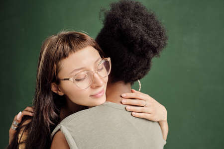 Happy amorous female embracing her girlfriend of African ethnicity over green backgroundの写真素材