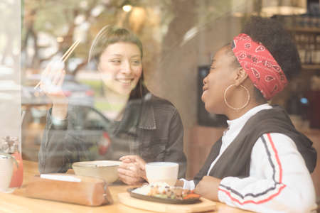 Two happy young intercutural females interacting during lunch in cafeの写真素材