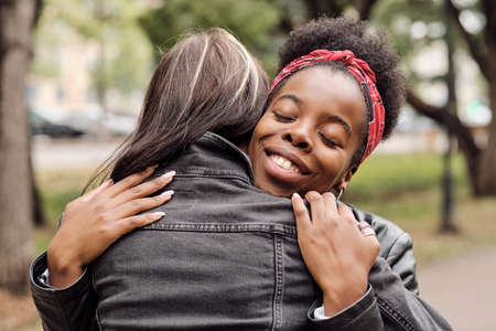 Happy young African female giving hug to her girlfriend in urban environmentの写真素材