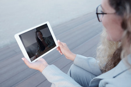 Young elegant businesswoman with tablet communicating with friend or colleague in video-chatの写真素材