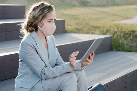 Young businesswoman in formalwear looking at screen of tablet while networking outdoorsの写真素材