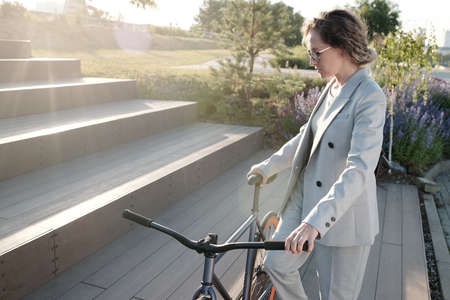 Young businesswoman with bicycle moving upstairs against public parkの写真素材