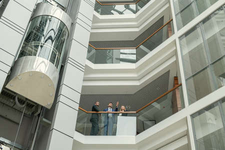 Business people standing at the balcony of modern office building and talking to each other during a...