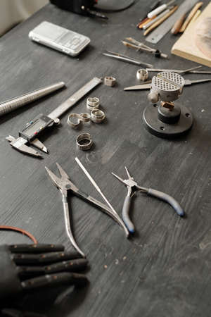 Close-up of jewelers tools including pliers and measuring tools placed on wooden table with ring...