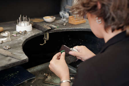 Over shoulder view of craftswoman using polisher while working with jewelry in workshop