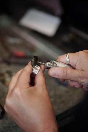 Hands of bench jeweler using abrasive polisher while crafting silver jewelry in workshop