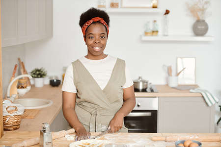 Young African housewife cutting homemade dough for pastry by kitchen tableの写真素材