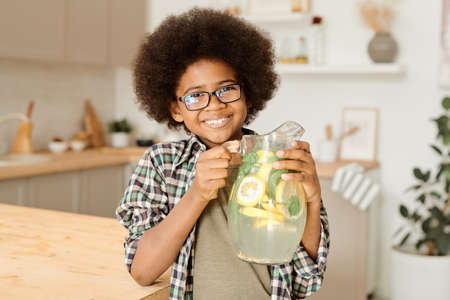 Cheerful little boy holding jug with homemade lemonade while standing in front of cameraの写真素材