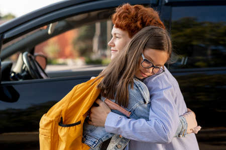 Mother and daughter standing in embrace against car outdoors in the morningの写真素材