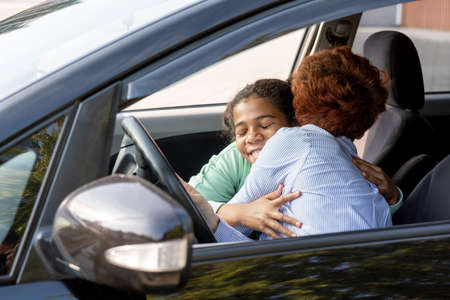 Happy schoolgirl embracing her mom before going to school while both sitting in the car