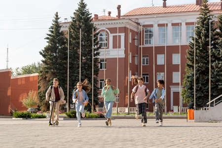 Happy schoolchildren running along large square while coming back from school on sunny dayの写真素材
