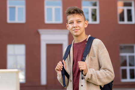 Contemporary youngster with backpack standing against building exterior and looking at youの写真素材