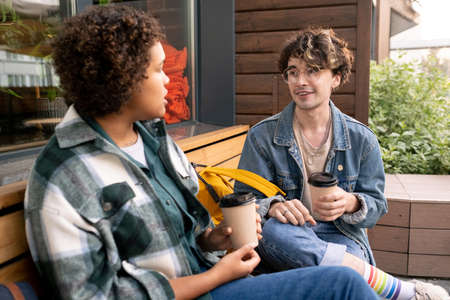 Happy teenage students in casualwear discussing college points after lessons outdoors