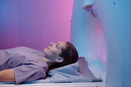Side view of young woman lying on table of mri scan machine and waitinf for beginning of medical...