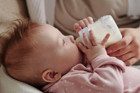 Side view of adorable baby girl eating milk from bottle against her motherの写真素材