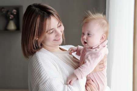 Young smiling female looking at adorable infant on her arms while standing in front of cameraの写真素材