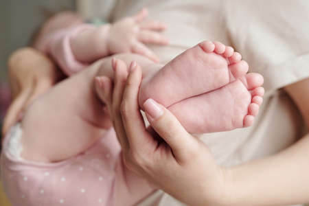 Hand of young woman holding bare feet of her cute sleeping baby daughterの写真素材