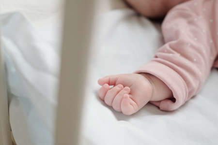 Small hand of cute infant in pink baby loose jacket sleeping in cribの写真素材