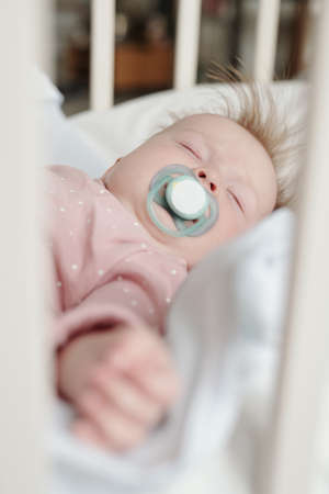 Peaceful infant with pacifier in mouth having rest in her crib in the middle of the dayの写真素材