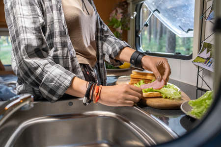 Hands of female putting bacon and lettuce on slice of wheat bread while making sandwichesの写真素材