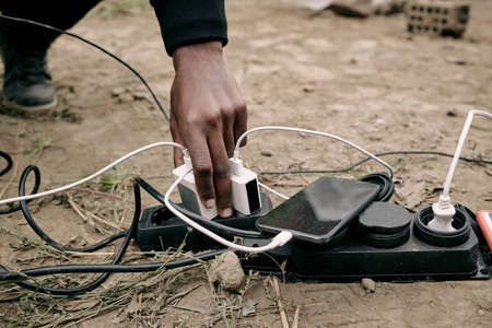 Close-up of unrecognizable black man plugging phone charger into socket on ground outdoorsの写真素材