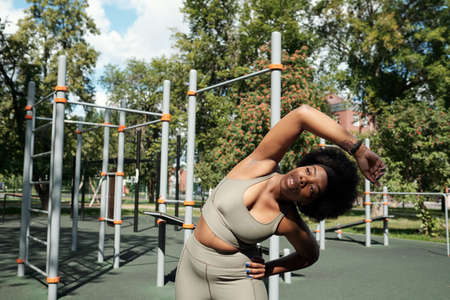 Active young sportswoman doing side bends against outdoor sports facilities