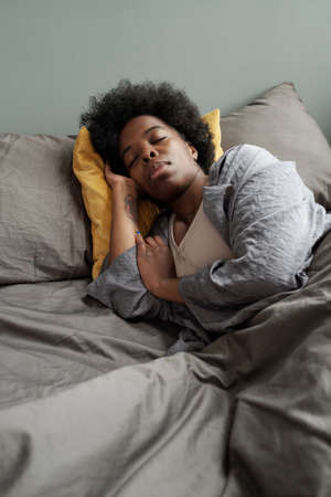Tired African woman lying under grey blanket in bed and napping
