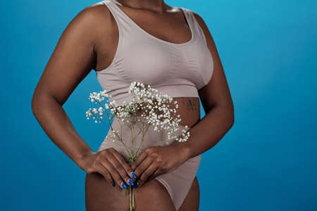 Body of young plus size woman of African ethnicity in underwear holding wildflowersの写真素材