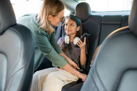 Young blond woman helping her cute little daughter fasten seat belt before drivingの写真素材
